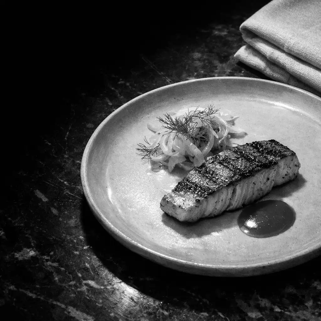 Charred fish plate with fennel fronds on a dark marble pass
